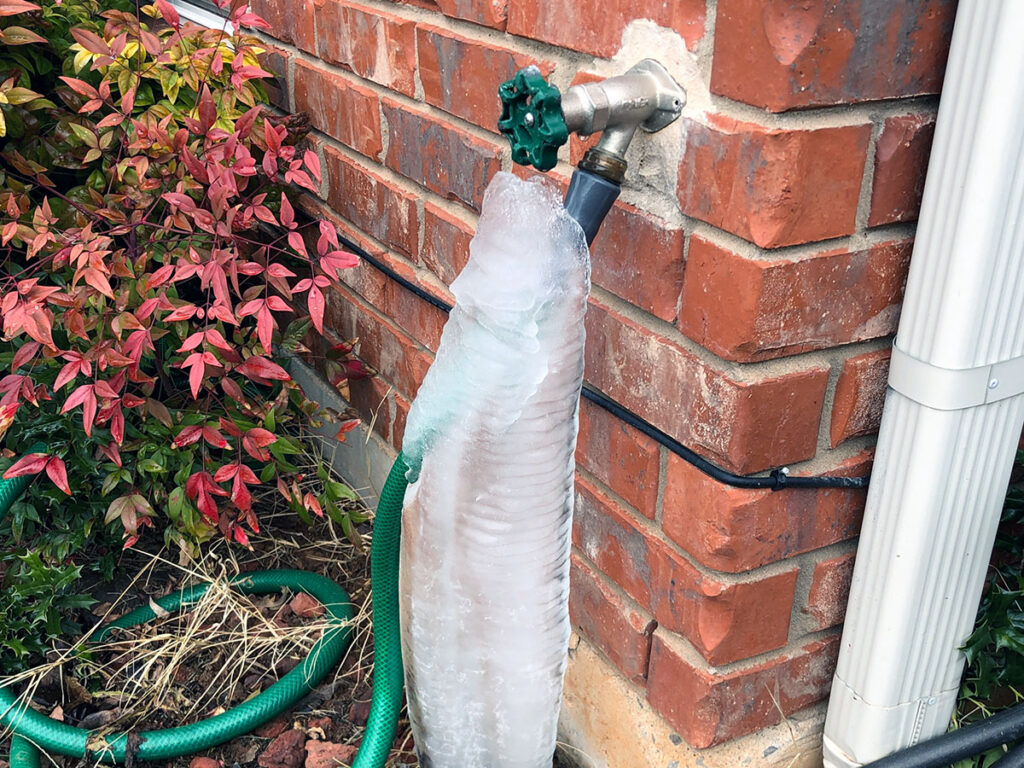 A PRV could have helped avoid the pressure in this outdoor hose pipe that froze and burst. Frozen ice runs down the hose. 